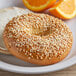 A bagel with Badia white sesame seeds on top on a plate with orange slices.