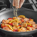 A person sprinkling Badia Sazon Tropical Seasoning on shrimp in a pan.