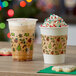 Two Choice 12 oz. plastic cups with holiday designs filled with coffee on a table next to a cookie.