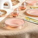 A close-up of a Visions blush plastic bowl with a gold rim on a table with pink plates and forks.