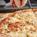 A hand sprinkling Badia Crushed Red Pepper on a pizza.