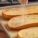 A hand sprinkling Badia Garlic Salt on a piece of bread.
