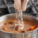 A person sprinkling Badia Onion Powder into a pot of stew.