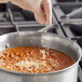 A person pouring Badia Chopped Onion into a pot of food.