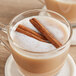 A glass mug of hot liquid with cinnamon sticks.