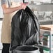 A man holding a Lavex black drawstring trash bag in a kitchen.