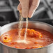 A person sprinkling Badia garlic powder into a pot of food.