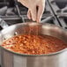 A gloved hand pouring Badia Chili Powder into a pot of food.