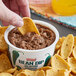 A person dipping a chip into a container of Furmano's Jalapeno Refried Bean Dip.