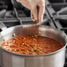 A person's hand pouring Badia ground cumin into a pot of food.