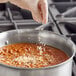 A person pouring Badia Chopped Onion seasoning into a pot of food.