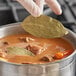 A person holding a Badia whole bay leaf over a bowl of soup.