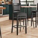 A Lancaster Table & Seating black wood bar stool with a black cushion on a restaurant table.