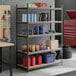 A black heavy-duty five-shelf boltless particle board shelving unit with various garage and automotive supplies stored on it.