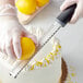 A person zesting a yellow fruit with a Choice stainless steel handheld zester with a black handle.