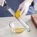A stainless steel grater zester with a black handle being used to zest a lemon over a glass bowl.