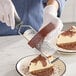 A stainless steel ribbon grater with a black handle being used to grate chocolate over a slice of cheesecake.