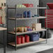 A black heavy-duty 4-shelf boltless particle board shelving unit with various containers and supplies stored on it.