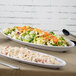 A white oval platter with salad and a fork on a table.