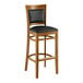 A wooden bar stool with a black vinyl cushion.