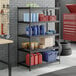 A black metal 5-shelf boltless wire shelving unit with various storage items placed on the shelves.