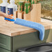 A hand using a Lavex blue duster to clean a black trash can.