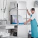 A man in a blue apron opening a Noble Warewashing tall dish washer in a professional kitchen.