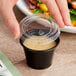 A hand holding a Choice black plastic souffle cup with a lid on a table.