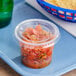 A clear plastic souffle cup with a lid of salsa on a blue tray.