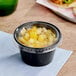 A small black plastic souffle cup with a clear lid on a table.