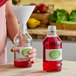 A woman pours red liquid into a clear glass juice bottle.