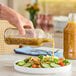 A hand pouring salad into a clear glass juice bottle.