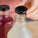 A hand holding a glass bottle with a black metal lid on it.