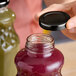 A person holding a 48 Lug black metal lid over a jar of juice.
