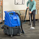 A man using a Lavex hard surface extractor with vacuum and solution hoses on a carpet.