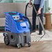 A man using a Lavex carpet extractor to clean a carpet with black hoses.