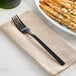 A Libbey stainless steel dinner fork on a napkin next to a plate of french fries.