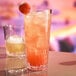 A Libbey Infinium Alto plastic highball glass filled with pink liquid and a strawberry on the rim.