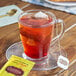 A glass cup of Celestial Seasonings Lemon Zinger tea with a tea bag on a saucer.