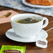 A cup of Celestial Seasonings green tea on a saucer with a tea bag in it on a table.