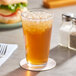 A glass of AriZona Lemon Iced Tea with ice sitting on a table next to a sandwich.