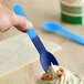 A hand holding a blue spoon over a cup of frozen yogurt.