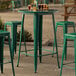 A Lancaster Table & Seating round emerald green table with green bar stools on a stone surface.
