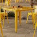 A Lancaster Table & Seating citrine yellow table and chairs on a stone patio.
