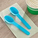 Two blue Choice heavy weight plastic spoons on a napkin next to a cup of ice cream.