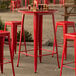A Lancaster Table & Seating Ruby Red Bar Height Outdoor Table with red bar stools on an outdoor patio.