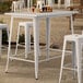 A Lancaster Table & Seating pearl white bar height outdoor table with drinks on it.