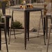 A Lancaster Table & Seating copper bar table with metal legs on an outdoor patio.