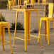 A Lancaster Table & Seating citrine yellow bar height table with a yellow metal bar.
