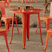 A Lancaster Table & Seating outdoor table and chairs set up on a stone patio with orange chairs.
